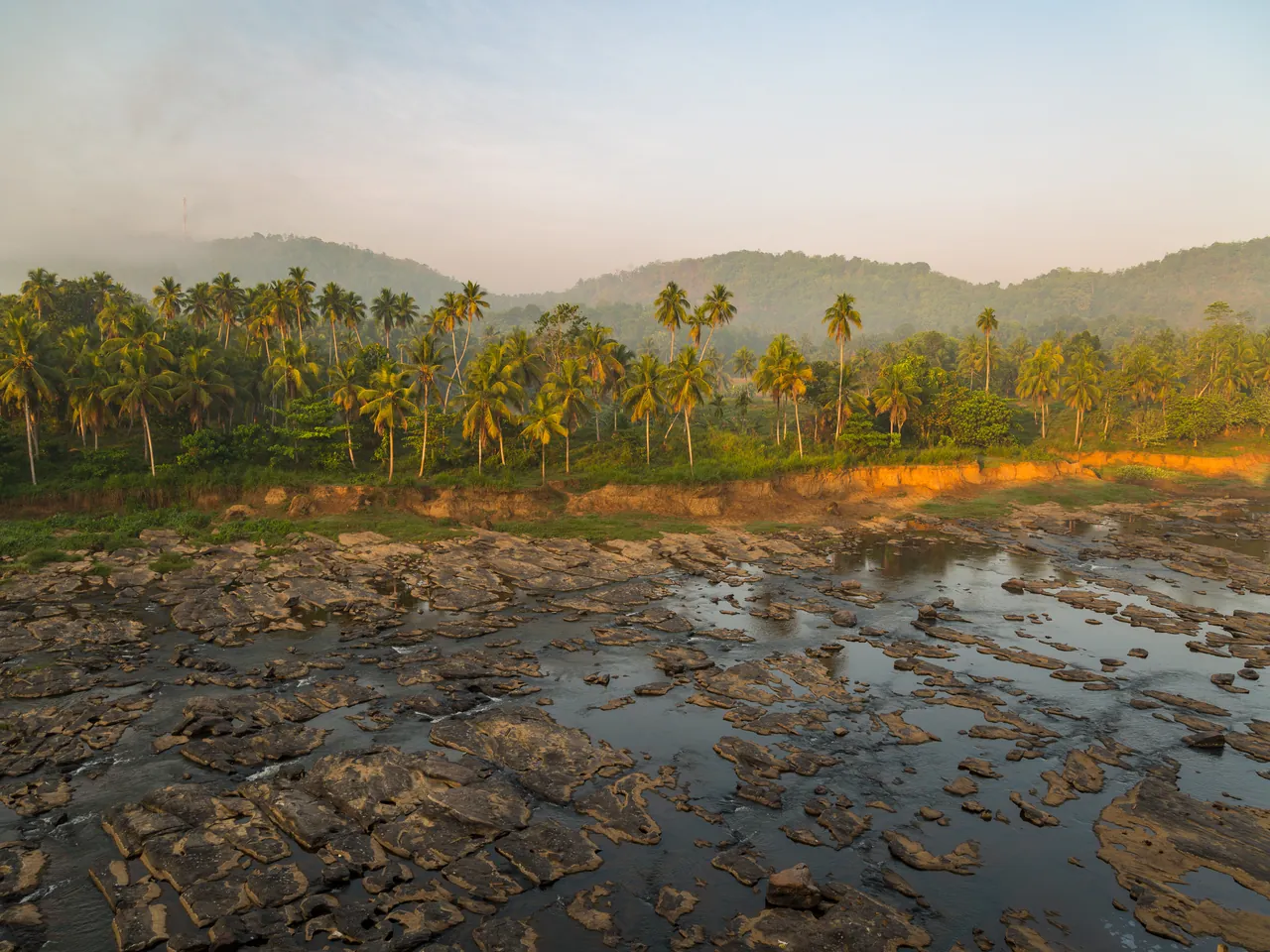 Golden evening light over the rocky Maha Oya River, framed by palm-covered hills in Sri Lanka.